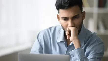 Man with a serious expression and hand to face looking at a laptop screen