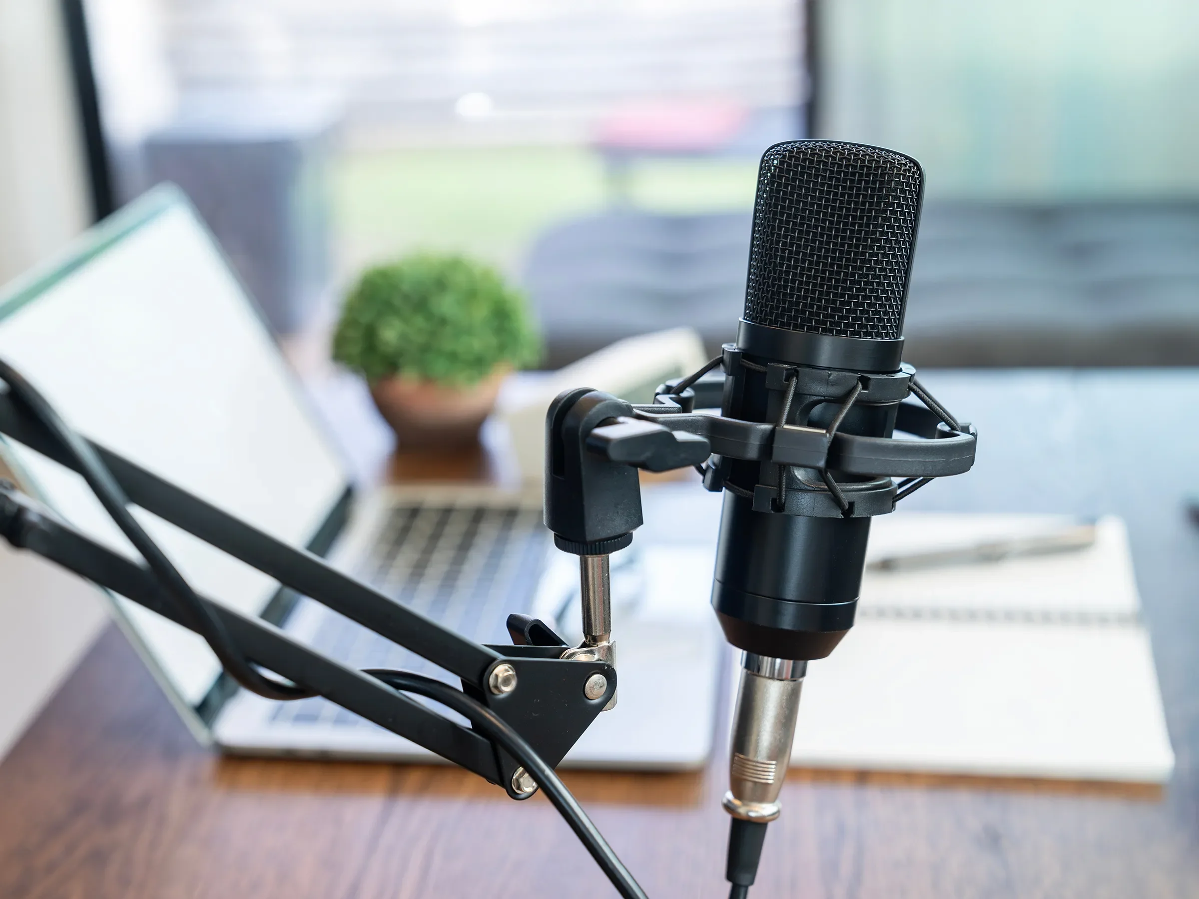 Podcast microphone at a desk in front of a laptop and notebook